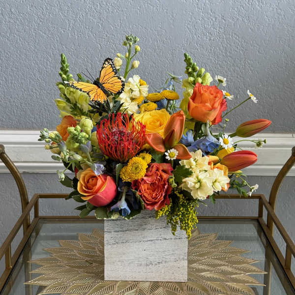 Mixed bouquet of orange, yellow, and white flowers in a square vase