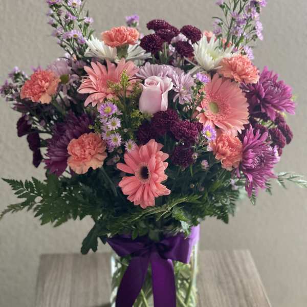 Mixed pink and purple bouquet in a glass vase with a purple ribbon