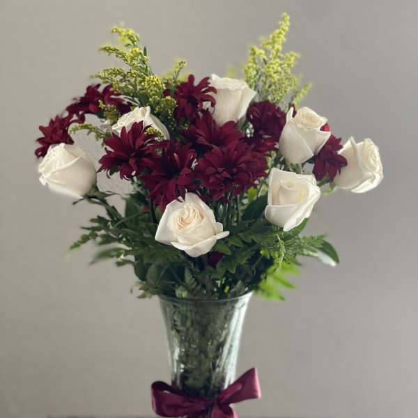 Bouquet of white roses and burgundy daisies in a glass vase with a ribbon