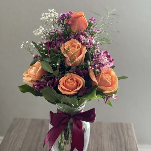 Peach roses and purple flowers in a glass vase with a ribbon