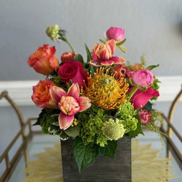 Mixed bouquet in a dark square vase with pink, orange, and green blooms