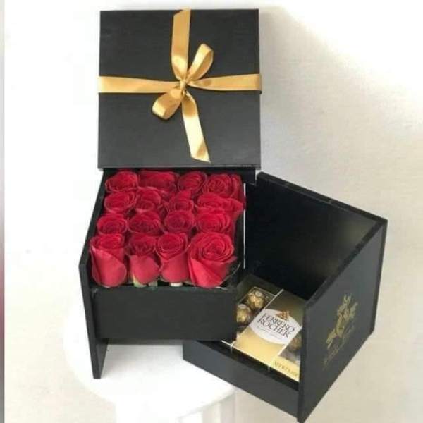 Black gift box with red roses and chocolates tied with a gold ribbon
