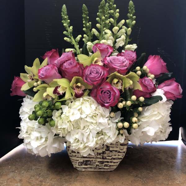 Pink roses and green orchids arranged with white hydrangeas in a patterned vase