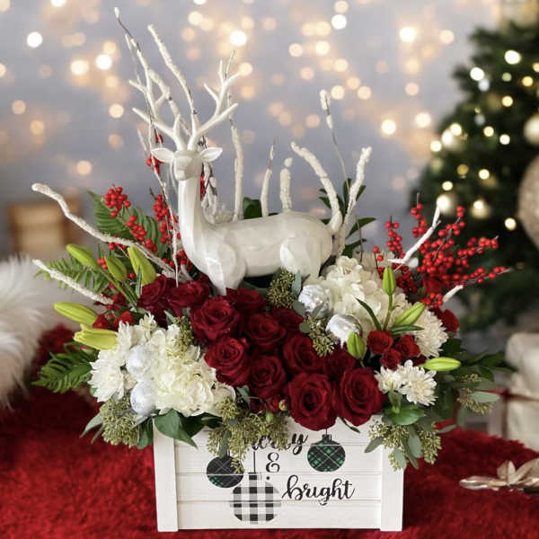 Holiday floral arrangement with red roses and a white deer figurine in a wooden box