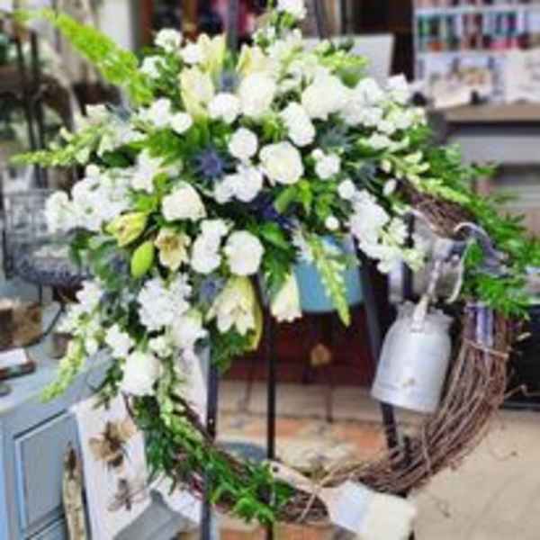 Large white floral wreath with trailing greenery and a silver watering can