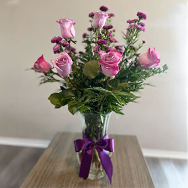 Pink roses in a clear vase with a purple ribbon