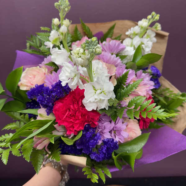 Mixed bouquet of pink, white, purple, and red flowers wrapped in purple paper