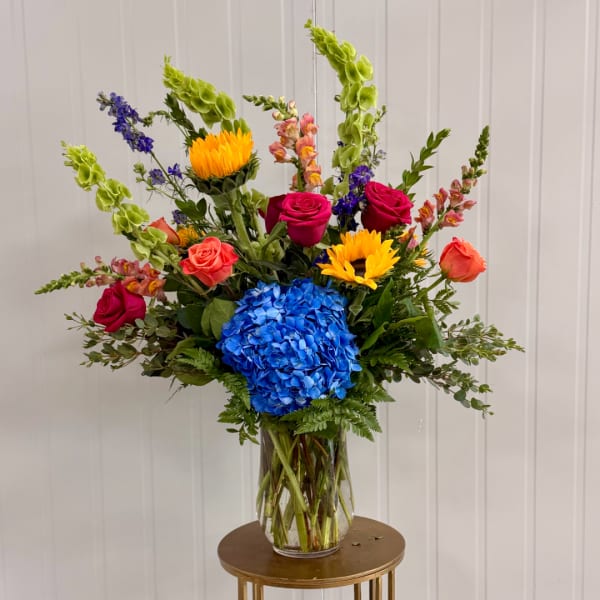 Colorful mixed bouquet in a clear glass vase with roses, hydrangea, and sunflowers
