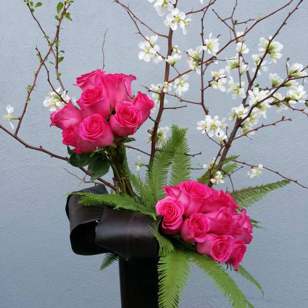 Pink roses in a tall black vase with white blossoms on branches