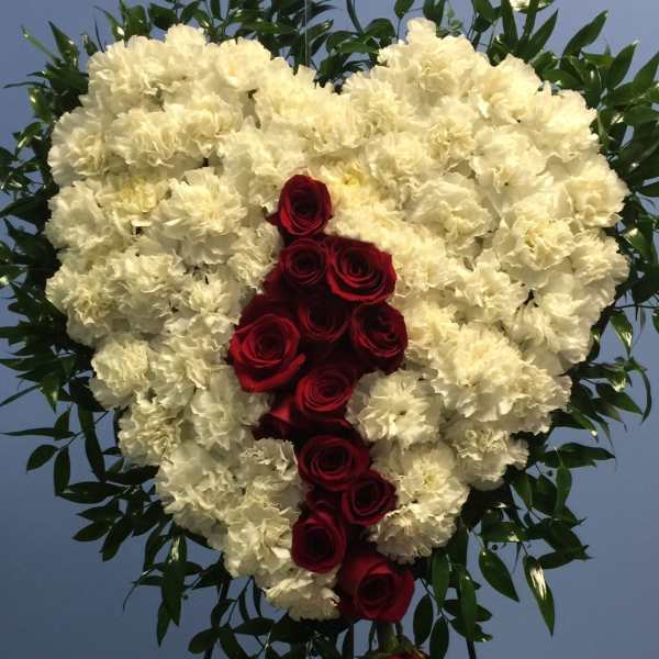 Heart-shaped standing spray of white carnations with cascading red roses on an easel.