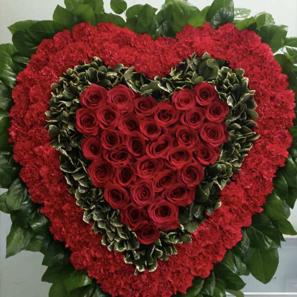 Heart-shaped red rose arrangement with red carnations and green foliage