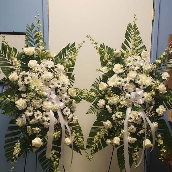 Two white floral standing sprays on easels with ribbon bows