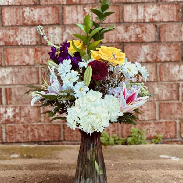 Mixed bouquet in a tall dark glass vase with yellow, white, purple, and pink flowers
