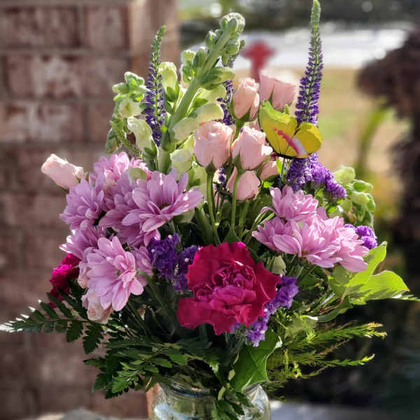 Mixed pink and purple flowers in a clear glass vase with a butterfly pick