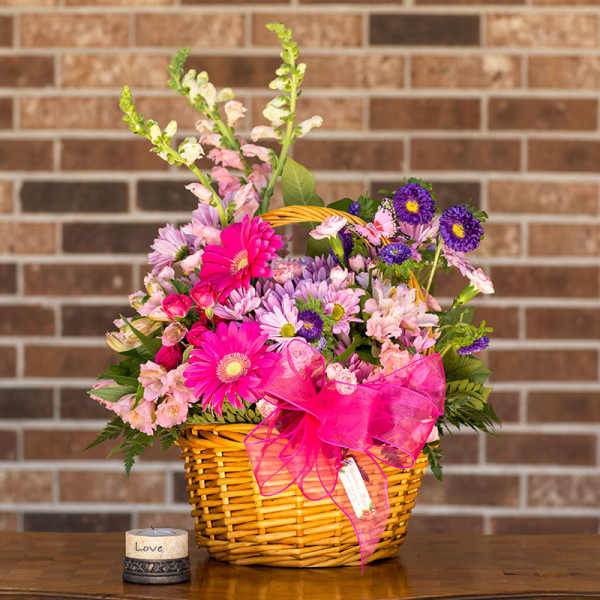 Pink and purple mixed flowers in a wicker basket with a bright ribbon