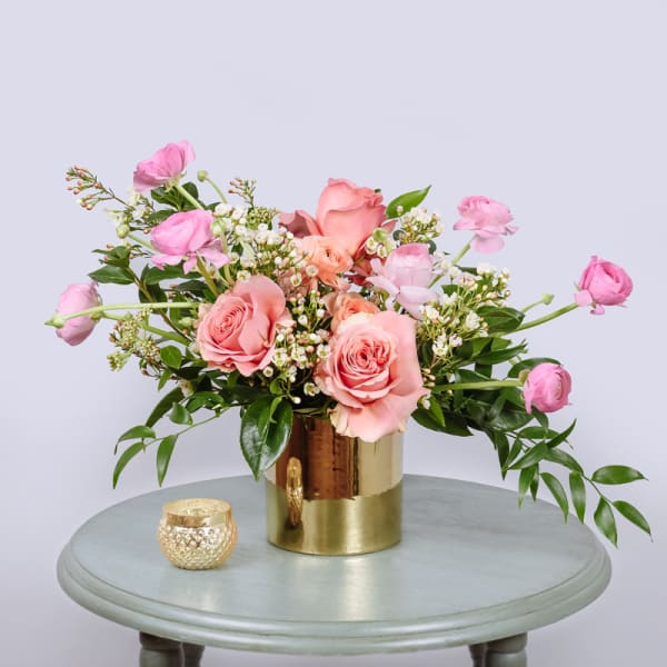 Pink roses and ranunculus in a gold vase with a small candle holder