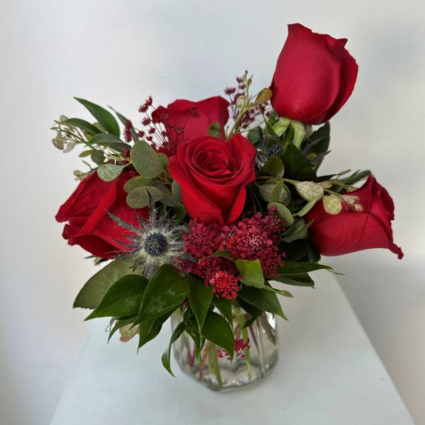 Red roses arranged in a clear glass vase with greenery and small accent flowers