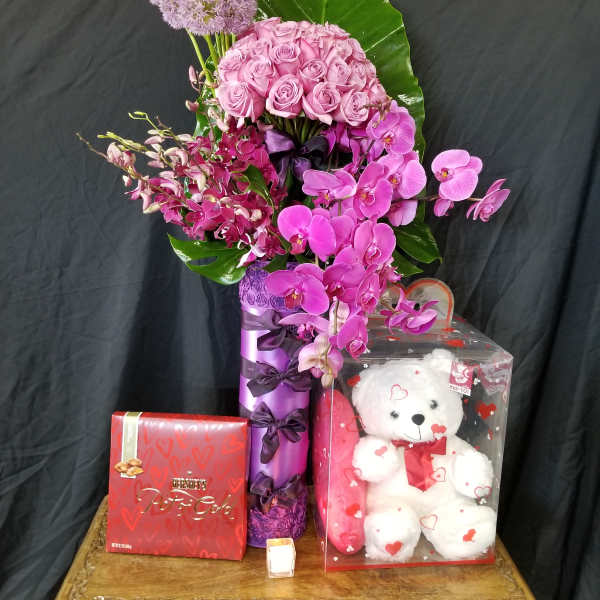 Pink roses and orchids arranged with a teddy bear and chocolates