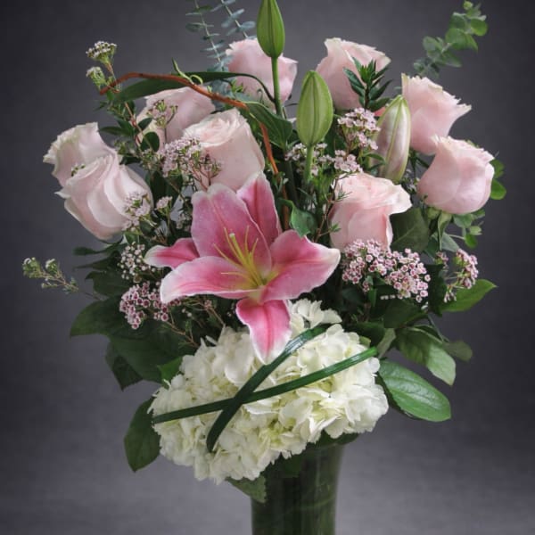 Pink lilies and roses arranged with white hydrangea in a glass vase