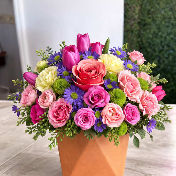 Bright mixed arrangement of pink roses, tulips and purple daisies in a terracotta cube vase