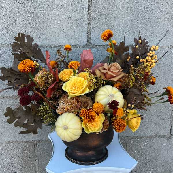 Autumn floral arrangement with yellow roses, marigolds, and small pumpkins in a dark vase