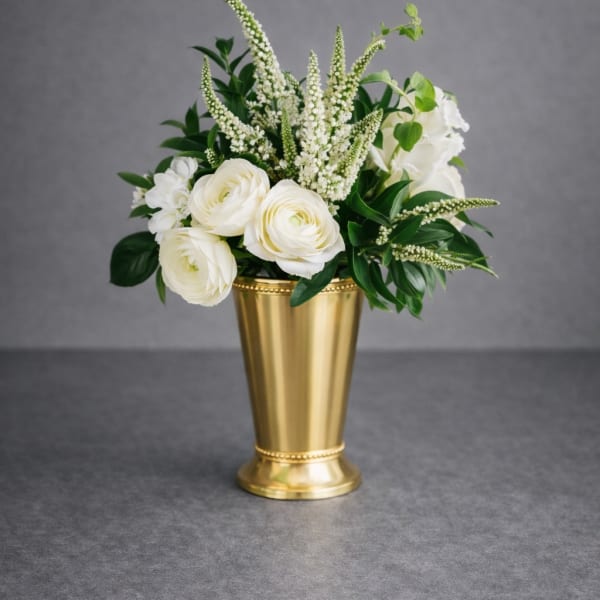 White flowers arranged in a gold vase with green foliage