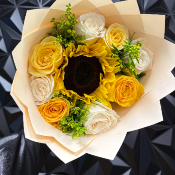 Handheld bouquet with a central sunflower surrounded by yellow and white roses in pale wrapping paper
