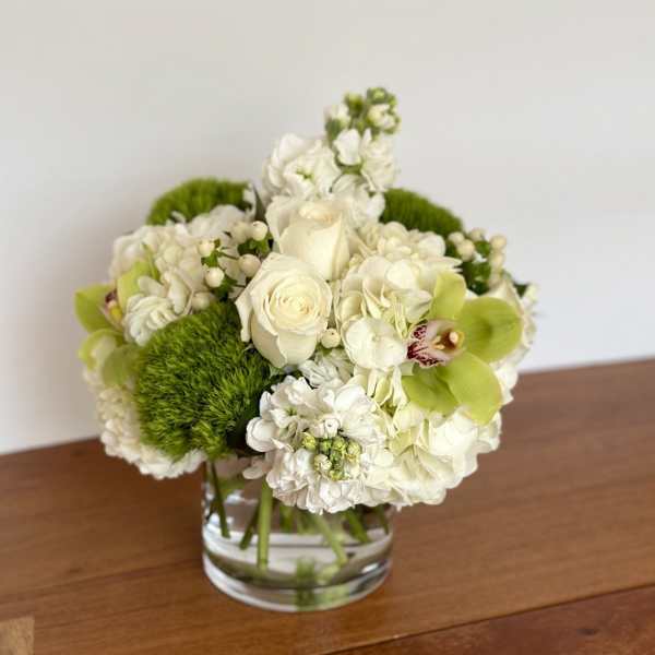 White floral arrangement in a clear glass vase with bright green accents