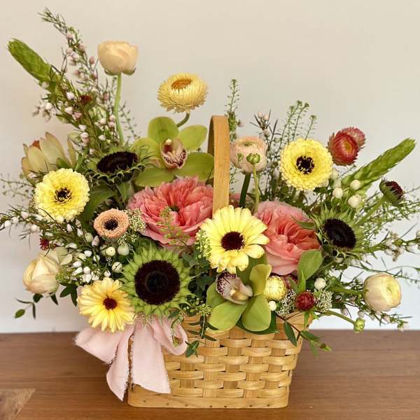 Mixed flower arrangement in a woven basket with a pink ribbon