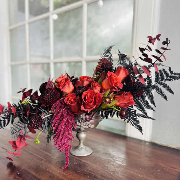 Red roses arranged in a silver pedestal vase with dark foliage