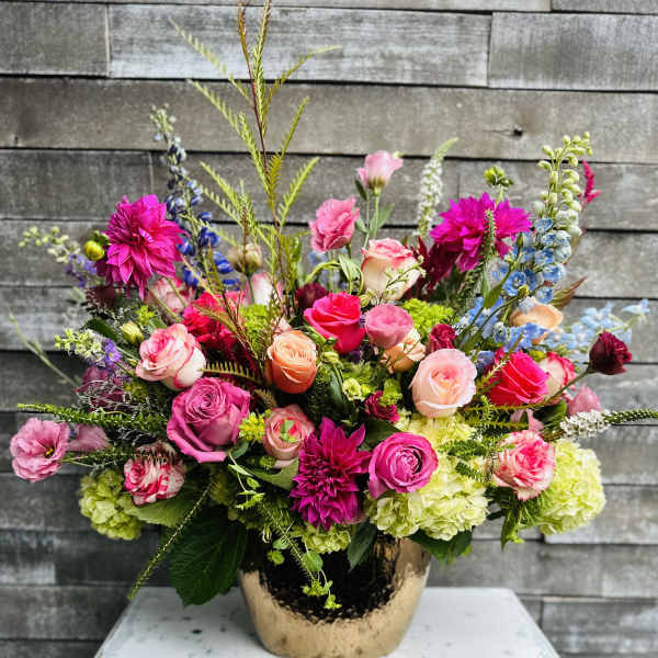 Bright mixed bouquet in a gold vase with pink, peach, and blue flowers