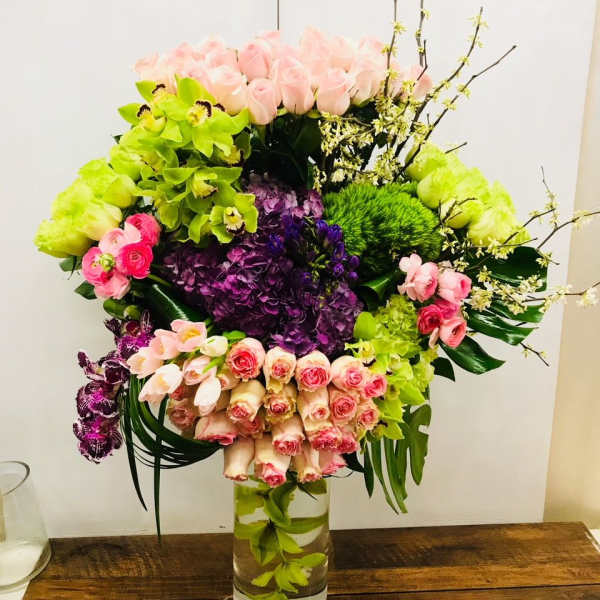 Large mixed bouquet in a clear glass vase with pink, green, and purple flowers