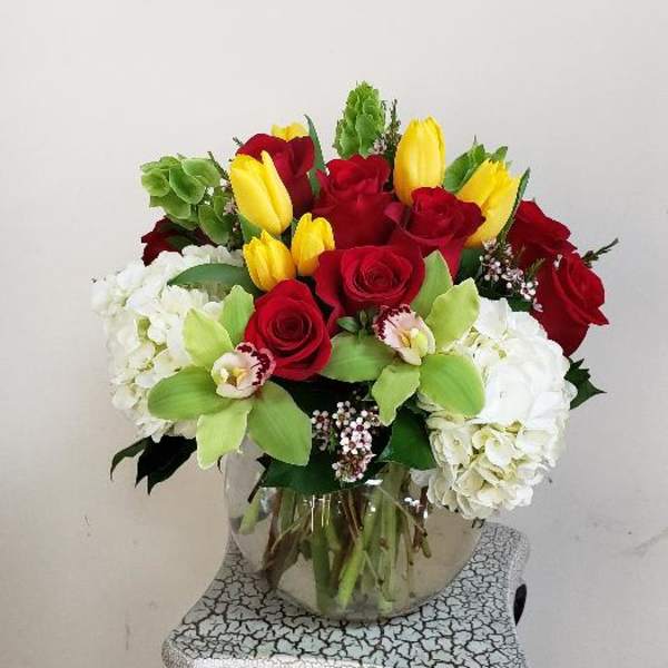 Bouquet of red roses, yellow tulips, and white hydrangeas in a glass vase