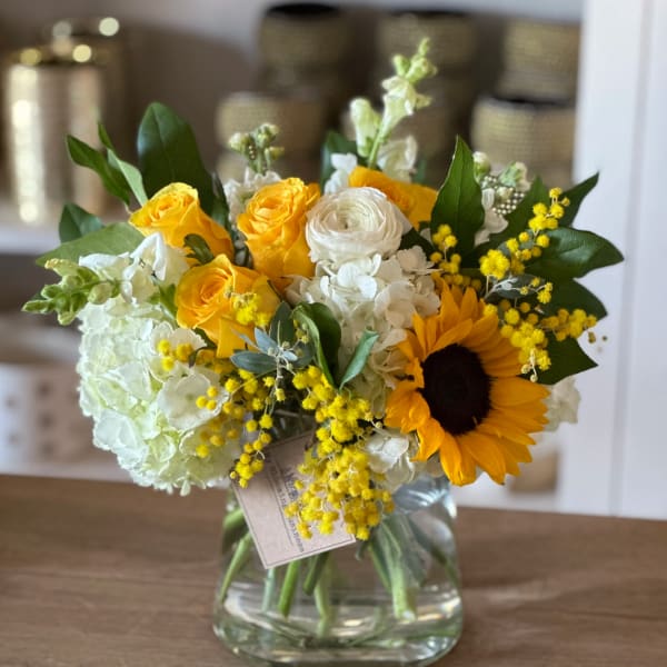 Bouquet of yellow roses, white blooms, and a sunflower in a glass vase