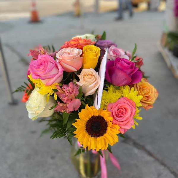 Mixed bouquet of colorful roses and a sunflower in a glass vase