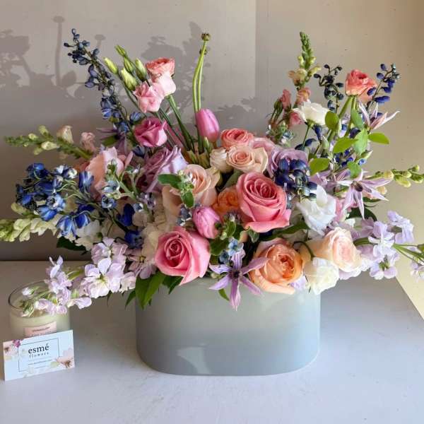 Pastel bouquet of roses, tulips, and blue flowers in a gray vase