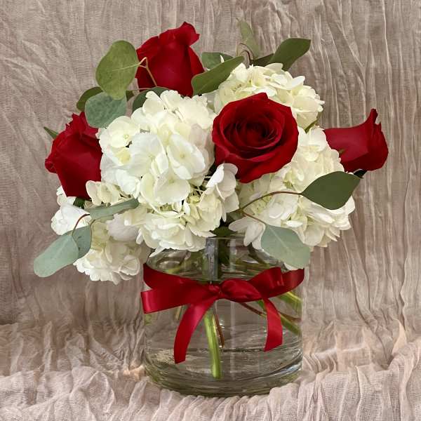 Red roses and white hydrangeas in a clear glass vase with a red ribbon