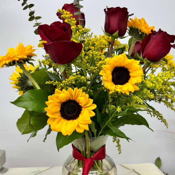Bouquet of red roses and yellow sunflowers in a glass vase with a red ribbon