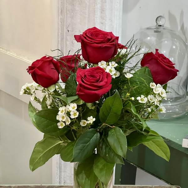 Red roses arranged in a clear glass vase with white filler flowers
