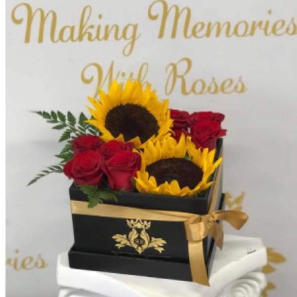 Sunflowers and red roses arranged in a black gift box with gold ribbon