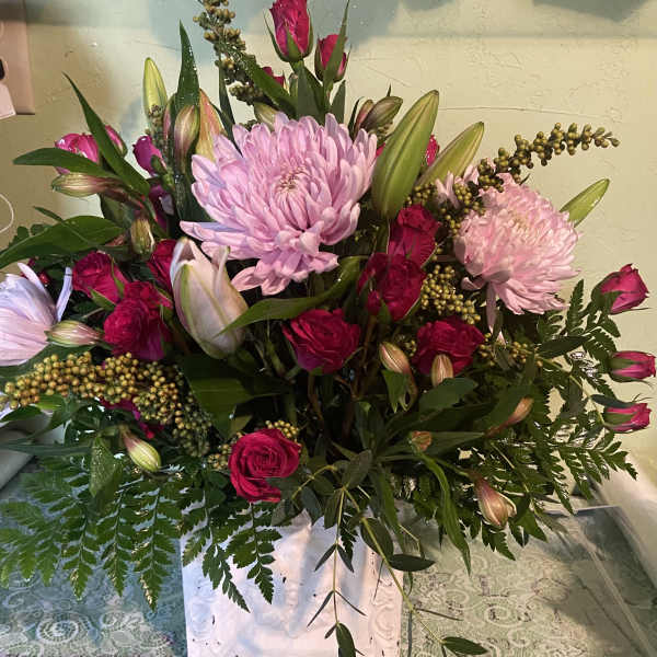 Pink roses and lilies arranged with large pink chrysanthemums in a white vase