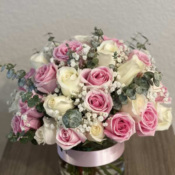 Pink and white roses arranged in a glass vase with eucalyptus