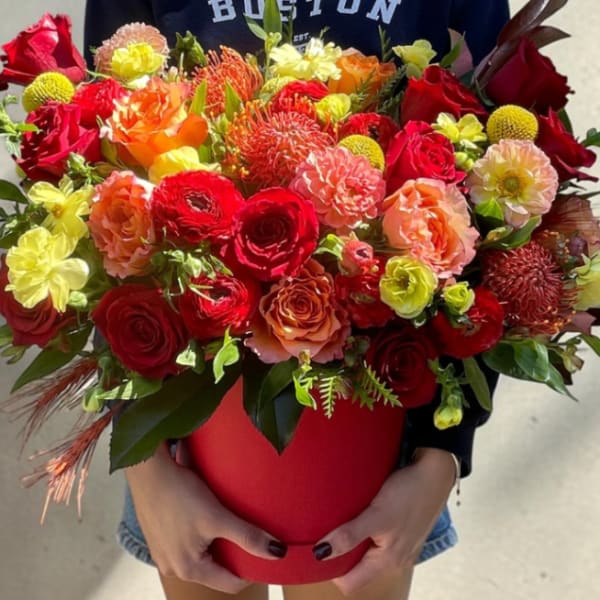 Large mixed bouquet in a red hatbox held by a person