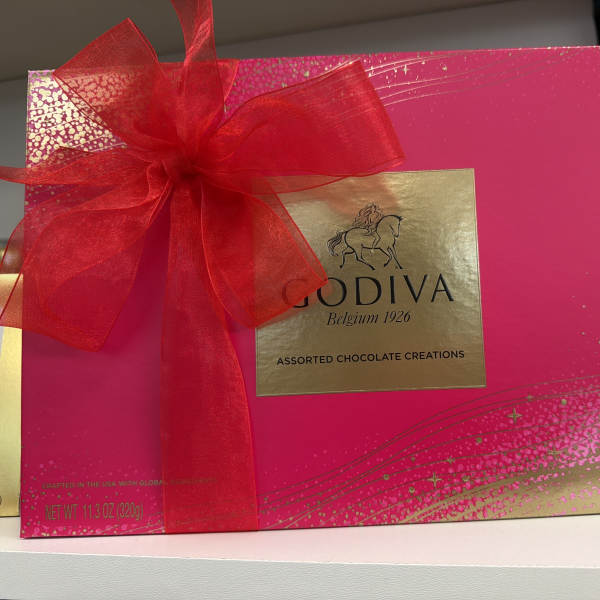 Bright pink Godiva assorted chocolates gift box with gold label and large red ribbon bow