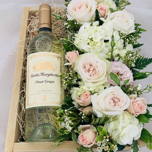 Wine bottle in a wooden gift box beside a pale pink and white flower arrangement