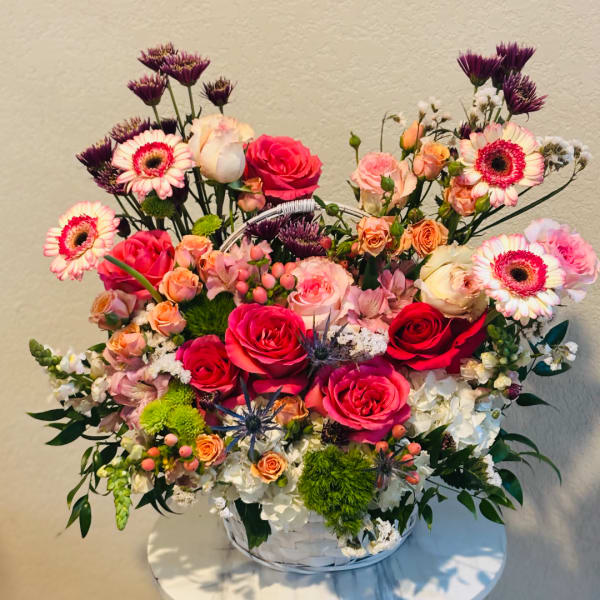 Mixed pink and peach floral arrangement in a white basket vase