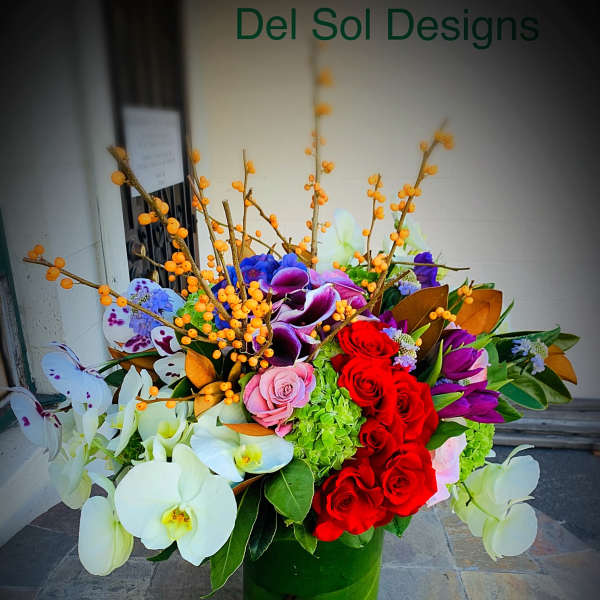 Large mixed floral arrangement in a green vase with orchids and roses