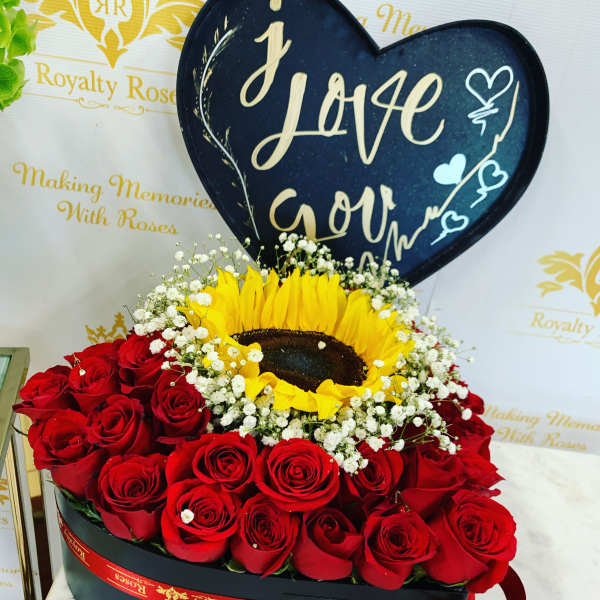 Heart-shaped sign above red roses and a sunflower in a black box
