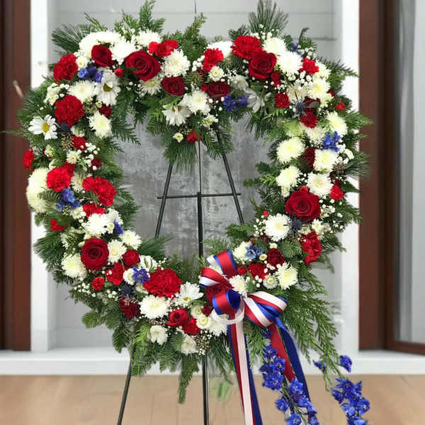 Heart-shaped floral wreath with red, white, and blue flowers on a stand