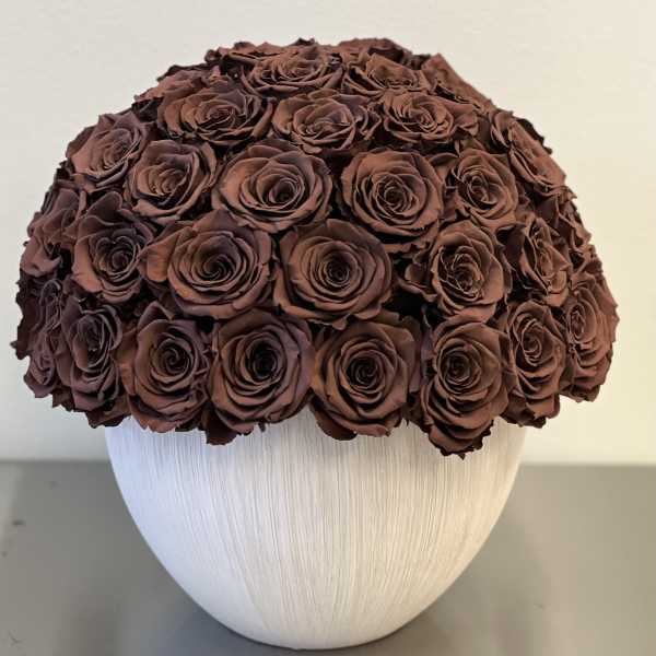 Round bouquet of dark brown roses in a white vase